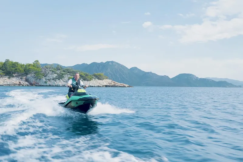 Koukles Yacht Photos Pics Man riding jet ski on blue ocean near rocky coastline, clear sky above.