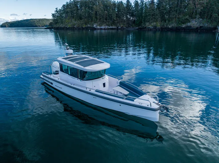 Windermere Yacht Photos Pics Axopar 28 boat, 2022 model, cruising on calm waters near a forested shoreline.