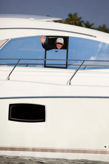  Yacht Photos Pics Person waving from a 2012 Prestige 440S yacht window, with palm trees in the background.
