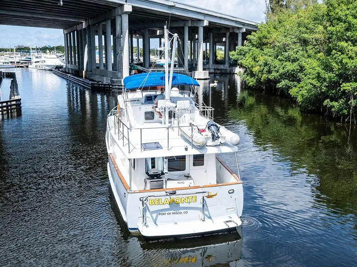  Yacht Photos Pics Selene Solo 2000 boat under bridge, calm water, lush greenery, blue canopy, rear view.