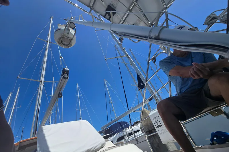 Georgia B Yacht Photos Pics Man sitting on a Hallberg-Rassy 42F Mk II sailboat, surrounded by masts, under clear blue sky.