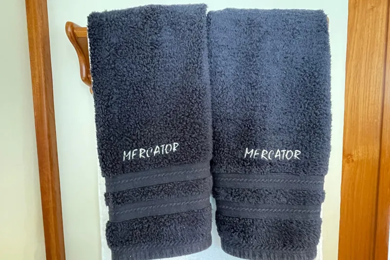 Mercator Yacht Photos Pics Dark blue towels with "Mercator" embroidery, hanging on a wooden rack.
