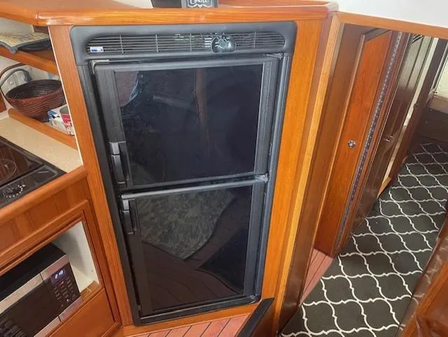 All Hans In Yacht Photos Pics 1999 Riviera SF interior with black refrigerator, wooden cabinetry, and patterned carpet.