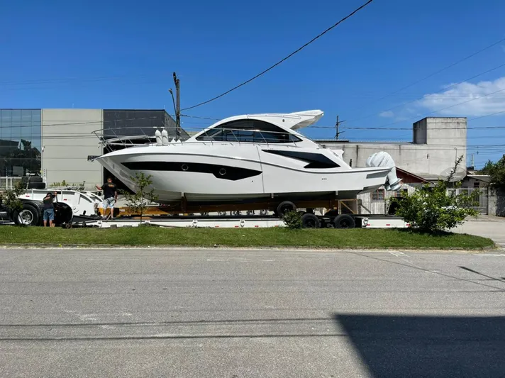 Seas The Moment Yacht Photos Pics Evolve 400HT 2021 yacht on trailer, parked near industrial buildings under clear blue sky.
