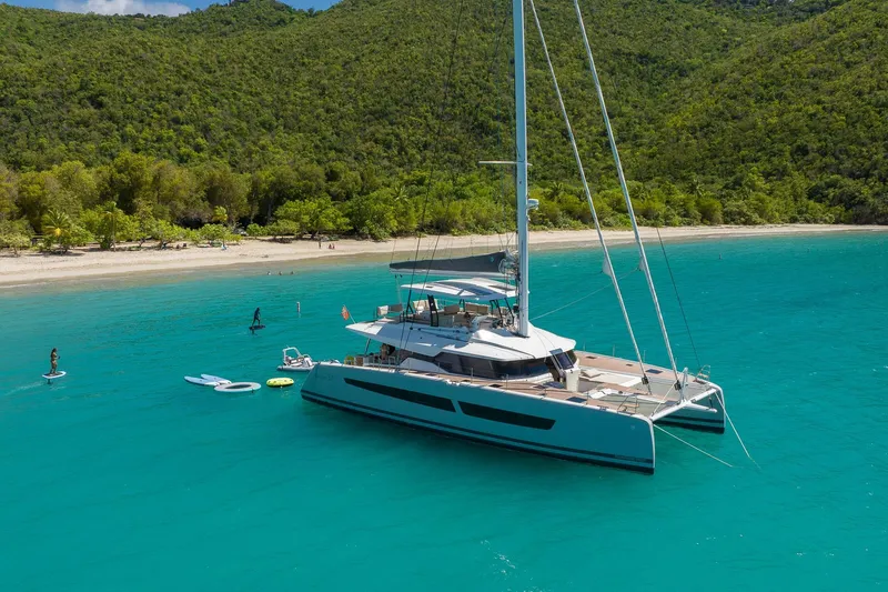 Jewel Yacht Photos Pics 2023 Fountaine Pajot Alegria catamaran anchored in turquoise waters near a lush, green coastline.