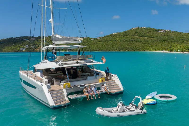 Jewel Yacht Photos Pics 2023 Fountaine Pajot Alegria catamaran anchored in turquoise waters, with people enjoying the sun.