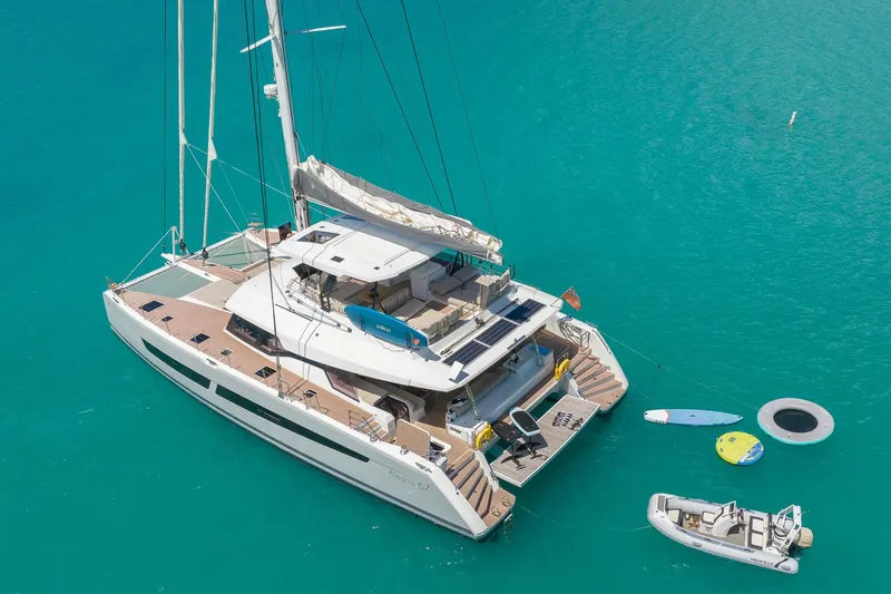 Jewel Yacht Photos Pics 2023 Fountaine Pajot Alegria catamaran on turquoise water, with water toys and a small boat.