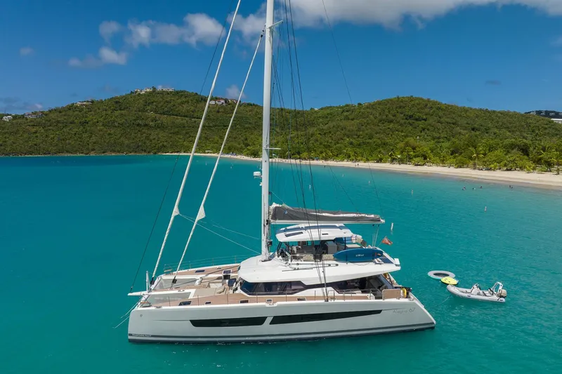 Jewel Yacht Photos Pics 2023 Fountaine Pajot Alegria catamaran anchored in turquoise waters near a lush green island.