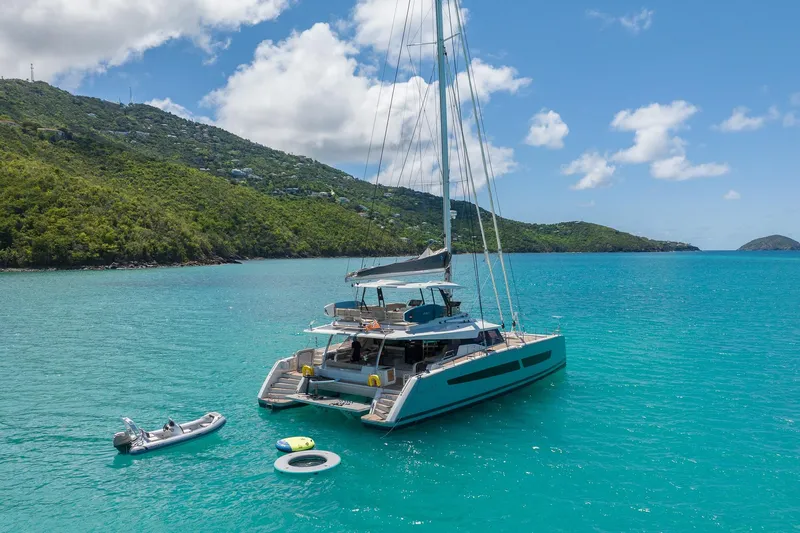 Jewel Yacht Photos Pics 2023 Fountaine Pajot Alegria catamaran anchored in turquoise waters, surrounded by lush green hills.