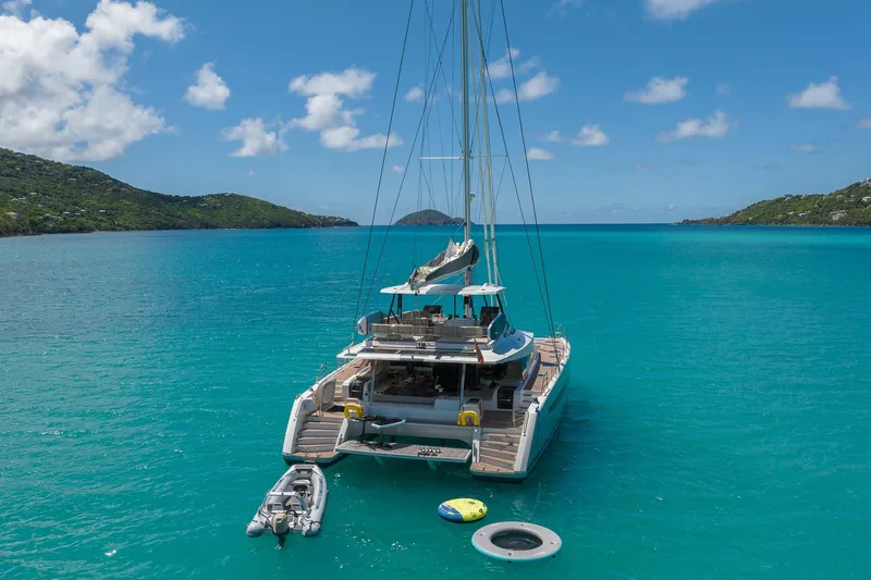 Jewel Yacht Photos Pics 2023 Fountaine Pajot Alegria catamaran anchored in turquoise waters, surrounded by lush green hills.