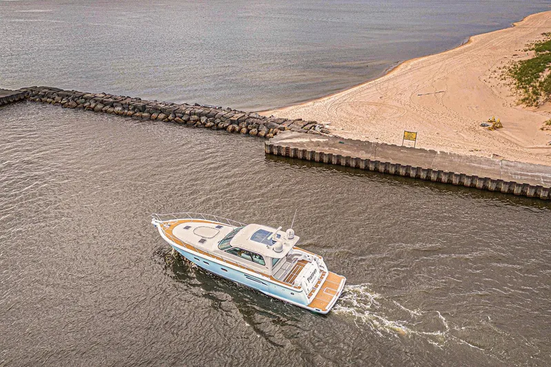 Playpen Yacht Photos Pics 2003 Tiara Yachts 5200 Sovran cruising near a sandy beach and rocky shoreline.