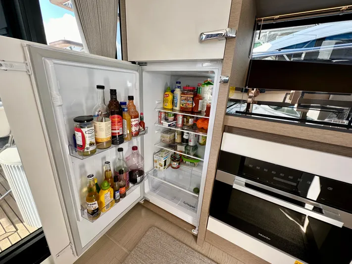 Pearl Voyage Yacht Photos Pics Open refrigerator in a 2023 Prestige 520 yacht, stocked with various beverages and condiments.