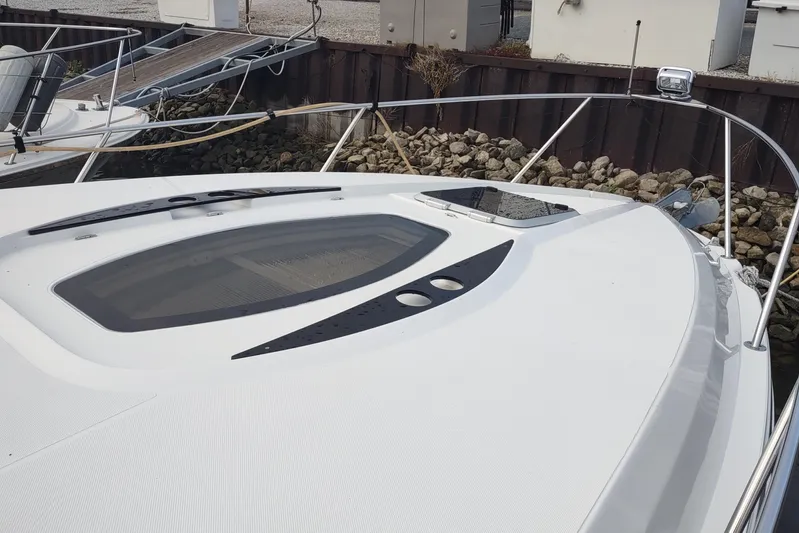  Yacht Photos Pics 2017 Rinker EX 320 boat bow with sleek design and deck hatch, docked by rocky shore.