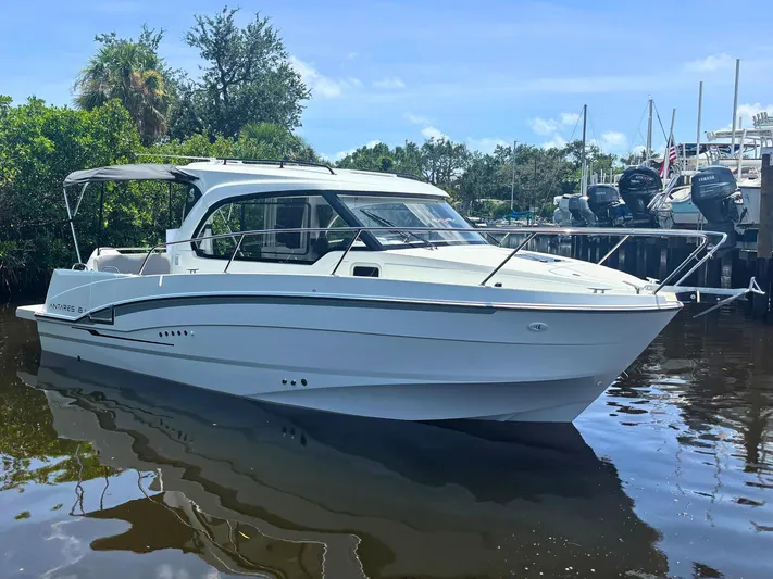  Yacht Photos Pics 2025 Beneteau Antares 8 boat docked on calm water, surrounded by lush greenery.