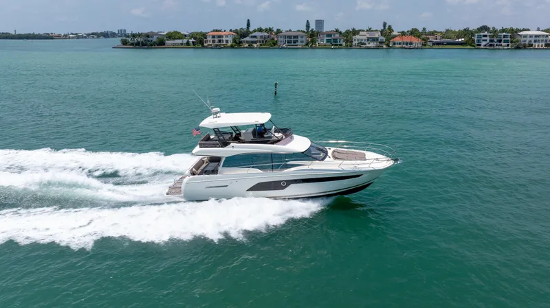 Motivated Seller Yacht Photos Pics 2019 Prestige 520 yacht cruising on turquoise waters near a coastal residential area.