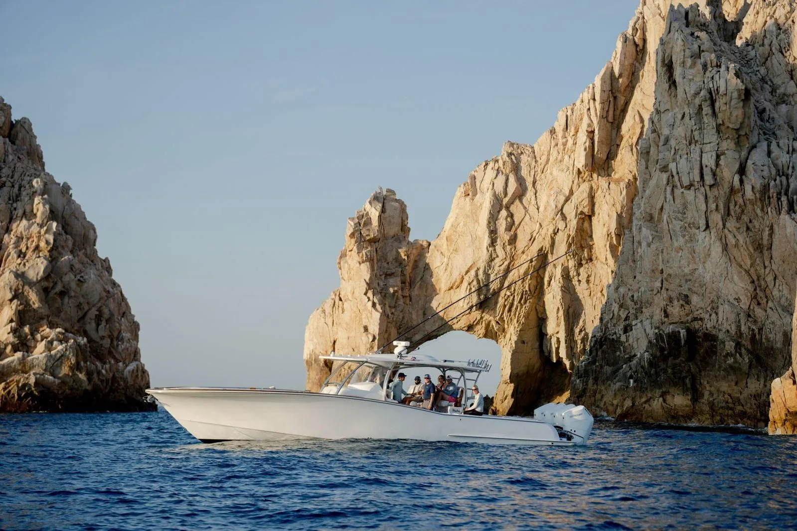 2024 Mag Bay 43 CC boat cruising near rocky cliffs in clear blue waters.