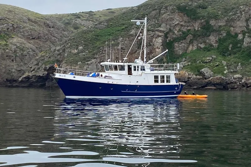 Blue Yacht Photos Pics 1989 Nordhavn 46 yacht anchored near rocky coastline with kayak nearby.