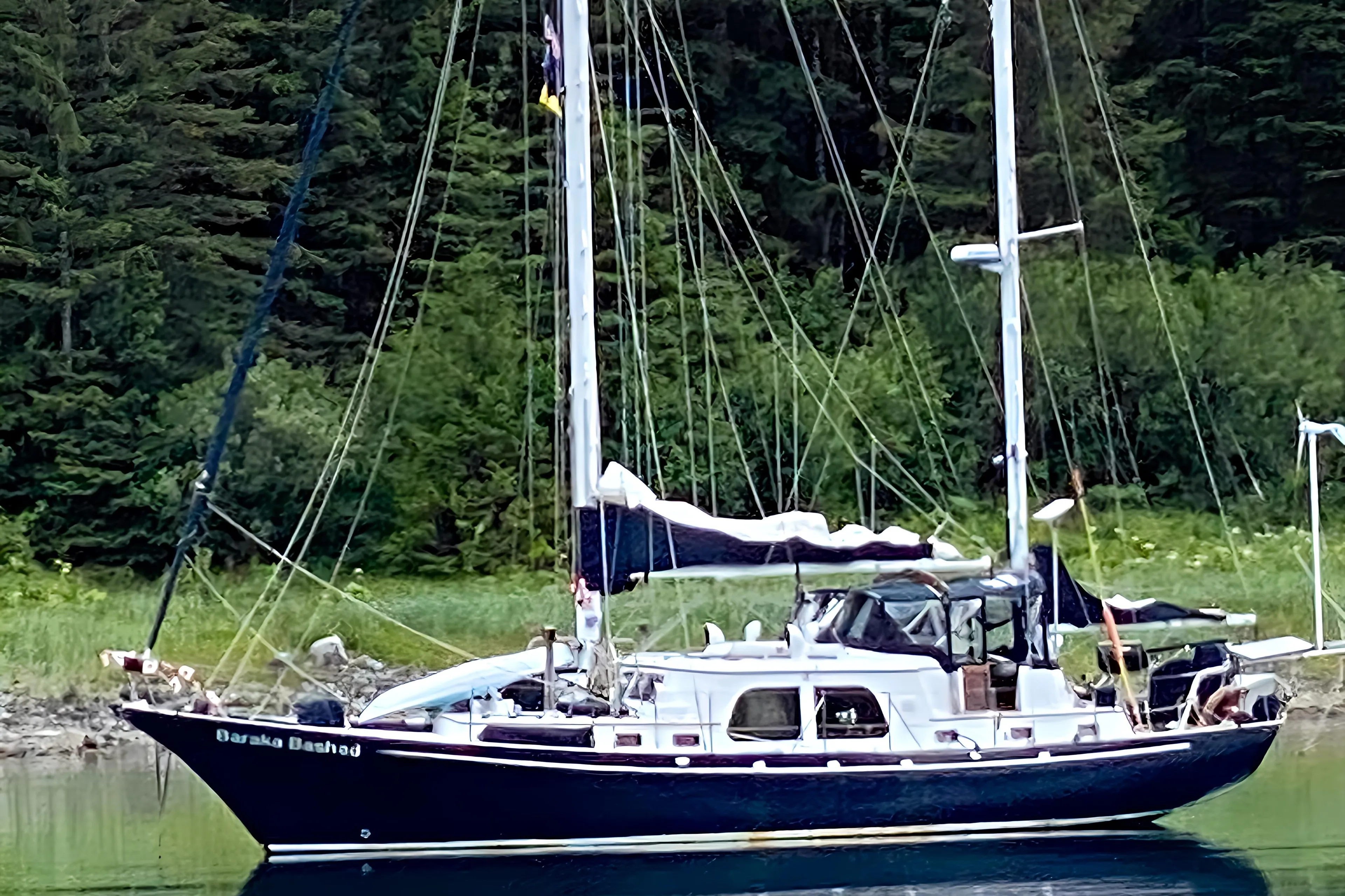 Custom 1969 Rhodes Motorsailer Steel Ketch anchored in a serene, forested bay.