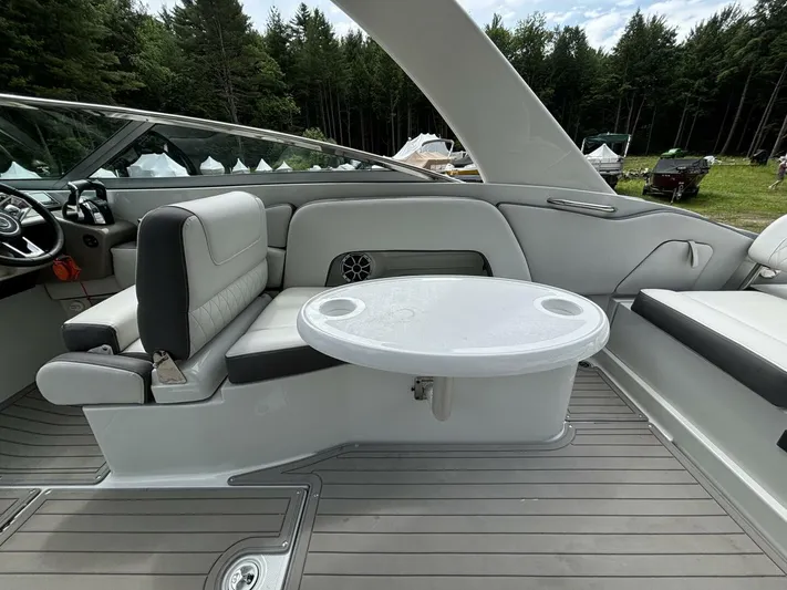  Yacht Photos Pics 2021 Crownline E305XS boat interior with seating and table, surrounded by lush forest.