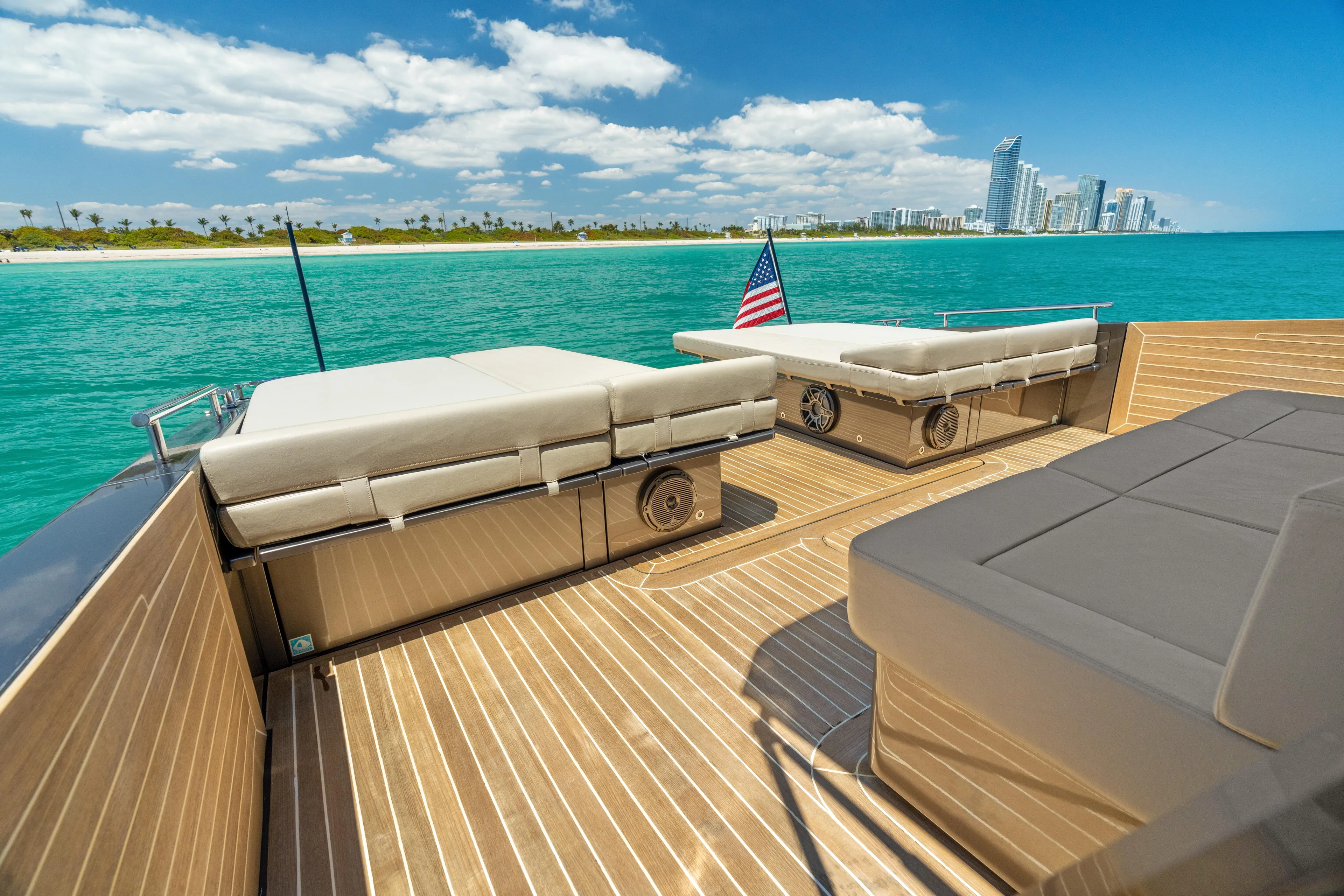 Yours Yacht Photos Pics Luxury yacht deck with sun loungers, ocean view, and city skyline in the background.