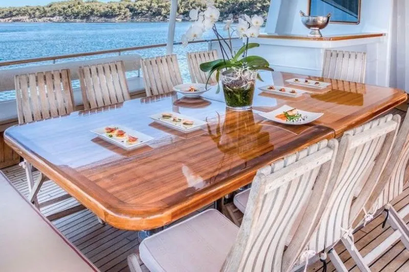 Clara One Yacht Photos Pics Luxurious yacht dining area with wooden table, elegant chairs, and scenic ocean view. Custom 90, 1961.
