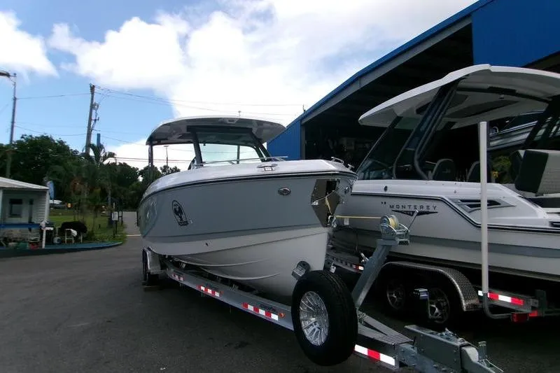  Yacht Photos Pics 2026 Monterey Elite 30 OB boat on trailer, parked outdoors near a blue building.