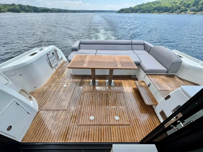  Yacht Photos Pics 2023 Prestige 520S yacht deck with wooden flooring, gray seating, and table, overlooking serene water.