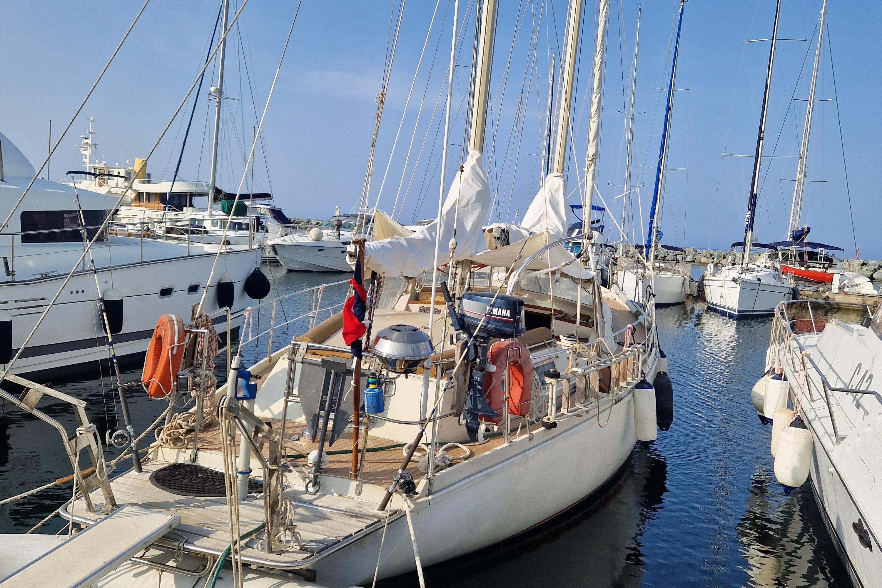 1982 Amel Maramu sailboat docked in a marina, surrounded by other boats.