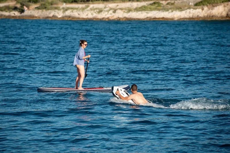  Yacht Photos Pics Woman paddleboarding and man swimming near shore, enjoying water activities.