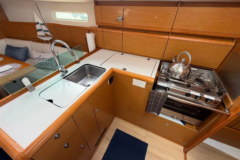 Layover Yacht Photos Pics Modern kitchen in 2018 Jeanneau Sun Odyssey 389 yacht with stove, sink, and wooden cabinetry.