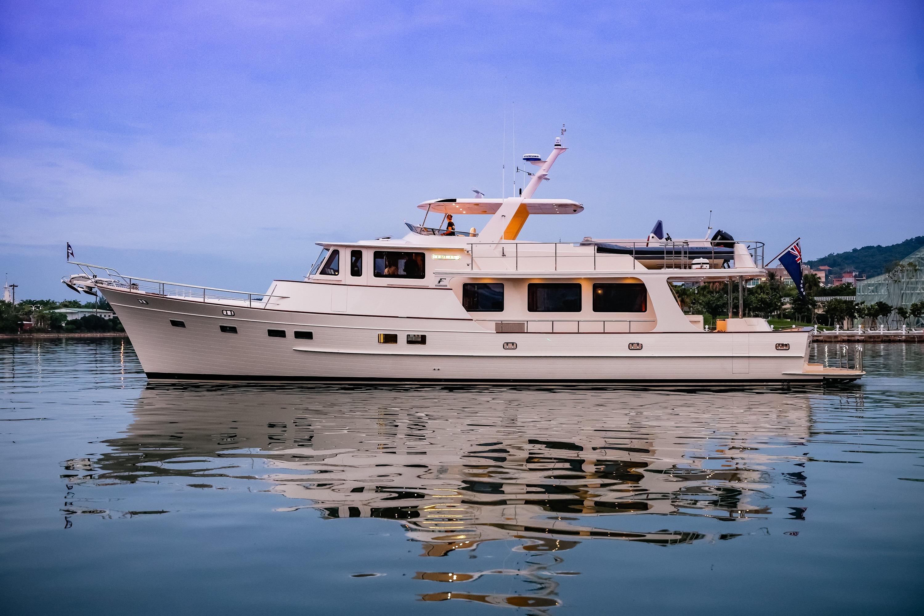 2027 Fleming 85 Pilothouse yacht on calm water, reflecting a serene sky.