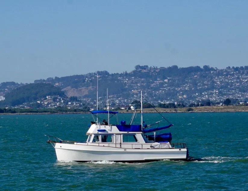 1982 Grand Banks Classic boat cruising on a scenic lake with hills in the background.