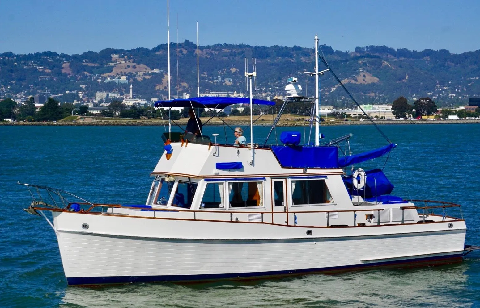 1982 Grand Banks Classic yacht cruising on a scenic waterway with hills in the background.