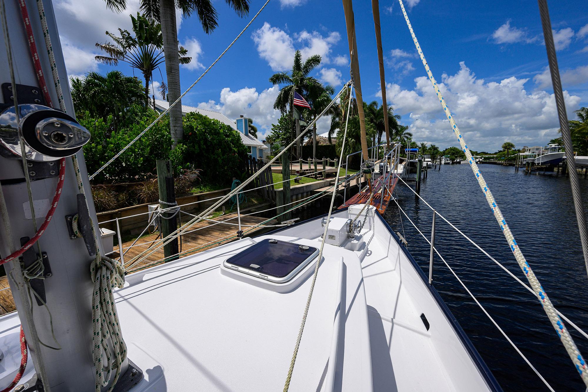 Schooner deck view with rigging, docked by palm trees under a blue sky.