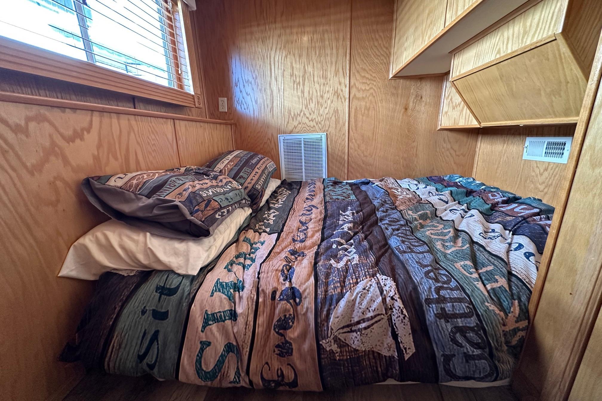 Cozy bedroom in 2004 Lakeview 16x68 houseboat with wooden walls and colorful bedding.