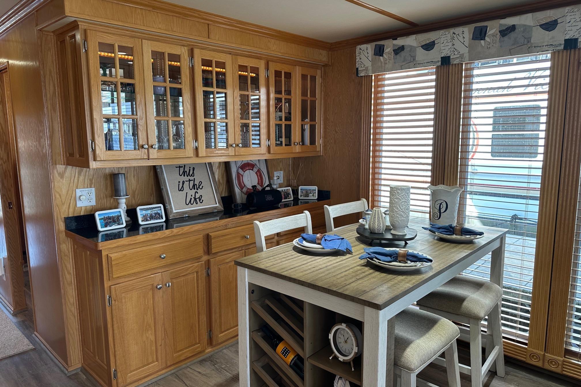 Dining area in 2004 Lakeview 16x68 houseboat with wooden cabinets and table setting.