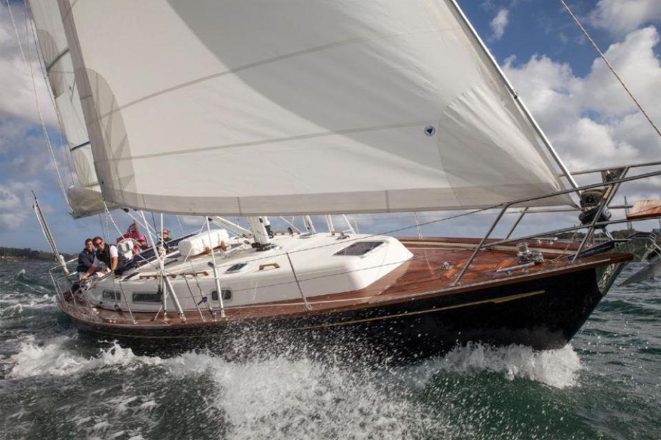 2025 Rustler 37 yacht sailing on open water with white sails and wooden deck.