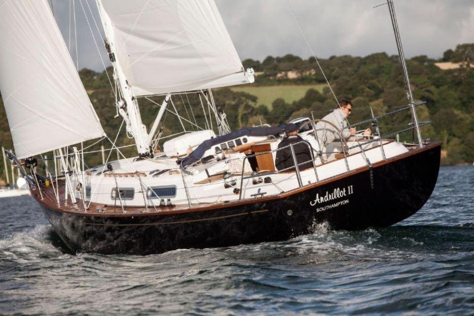 Sailing yacht Rustler 37, 2025 model, navigating coastal waters with lush green hills in background.