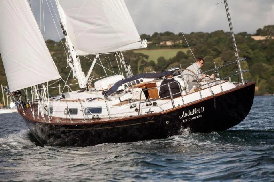 Sailing yacht Rustler 37, 2025 model, navigating coastal waters with lush green hills in background.