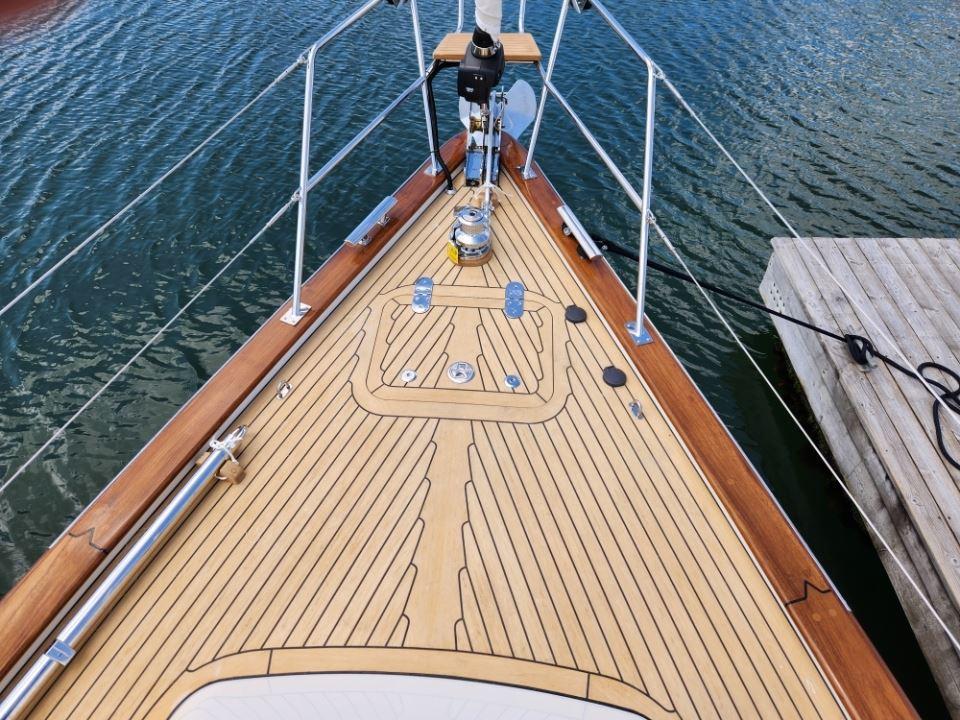 Bow of 2025 Rustler 37 yacht with teak deck, docked by water.