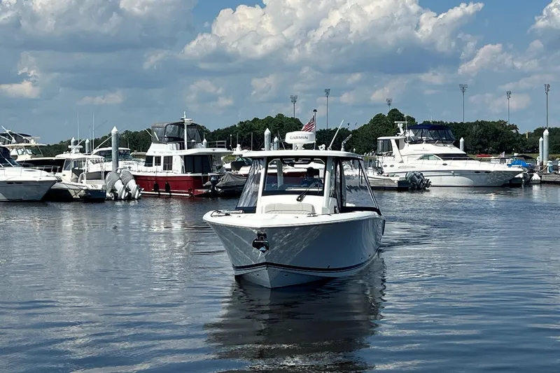  Yacht Photos Pics 2024 Pursuit S 328 Sport boat cruising in a marina under a partly cloudy sky.