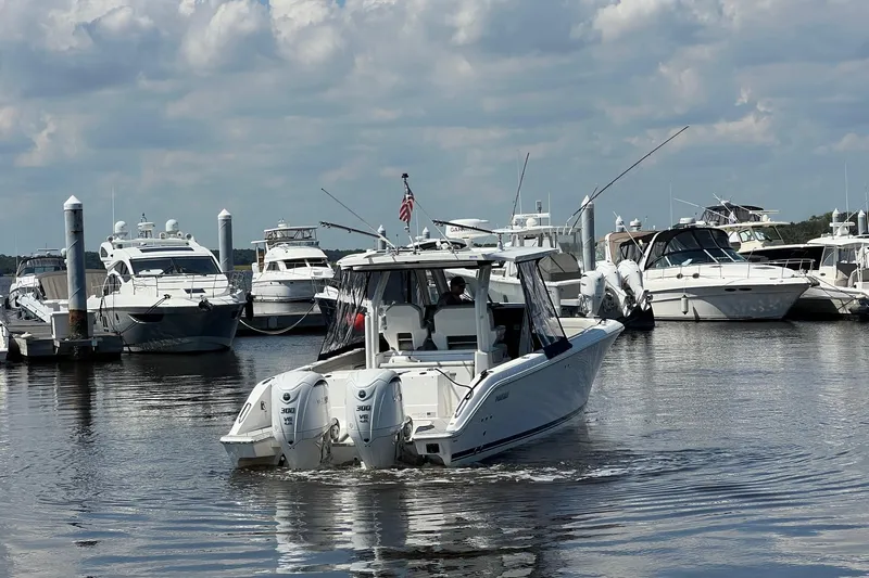  Yacht Photos Pics 2024 Pursuit S 328 Sport boat navigating marina with other yachts docked nearby.