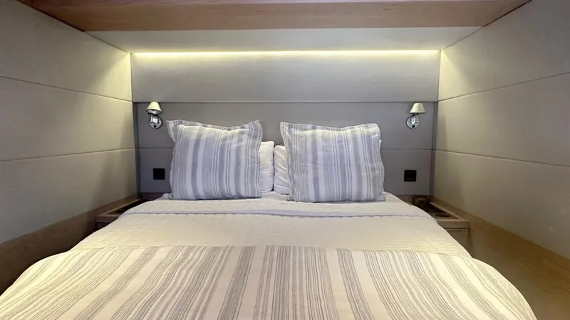  Yacht Photos Pics Luxurious bedroom interior of 2022 Lagoon 65 yacht with modern lighting and striped bedding.