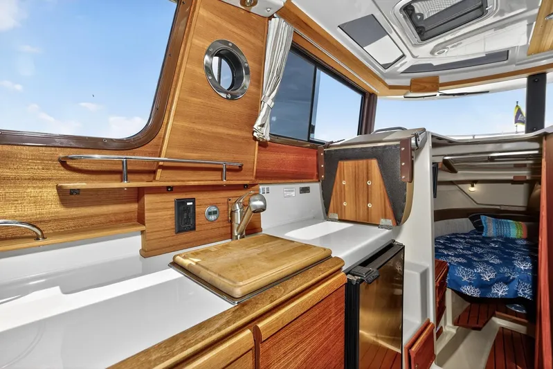  Yacht Photos Pics 2024 Ranger Tugs R-27 interior with wooden cabinetry, compact kitchen, and cozy sleeping area.