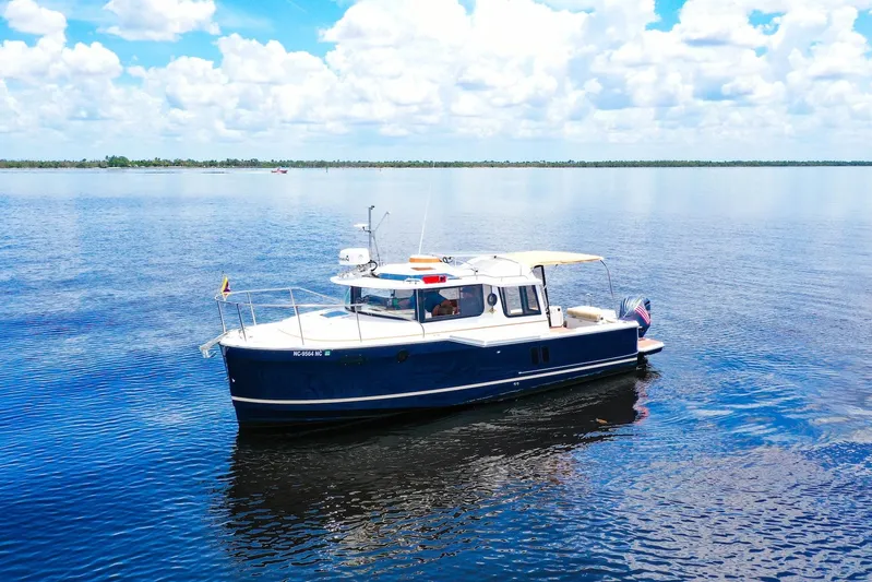  Yacht Photos Pics 2024 Ranger Tugs R-27 boat cruising on a calm lake under a blue sky.
