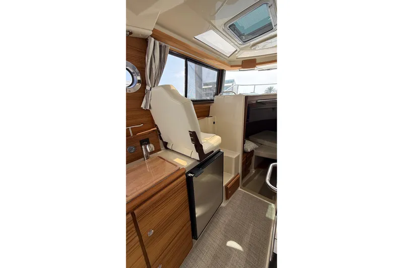  Yacht Photos Pics Interior of 2026 Ranger Tugs R-27, featuring seating, wood cabinetry, and a compact refrigerator.