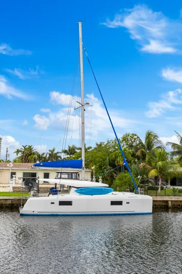 Benedetto Yacht Photos Pics 2020 Lagoon 42 catamaran docked by a waterfront home under a clear blue sky.
