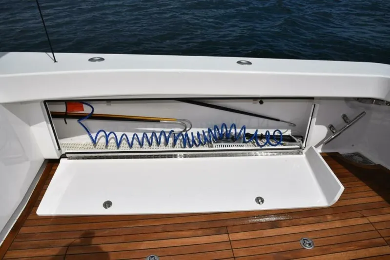 Another Day In Paradise Yacht Photos Pics Storage compartment on 2017 Viking 80 Sky Bridge yacht with coiled hose and wooden deck.