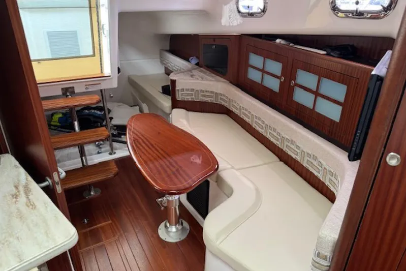 Nothing But Fine Yacht Photos Pics 2022 Pursuit OS 385 Offshore cabin interior with wooden finishes and seating area.