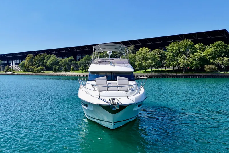  Yacht Photos Pics 2023 Prestige 460 yacht on clear blue water near a modern building and lush trees.